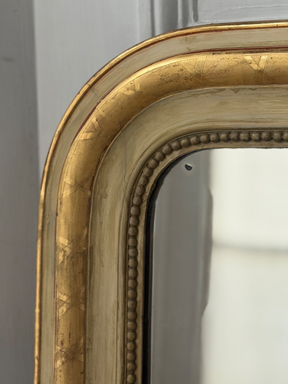 An antique Louis Philippe mirror with rounded upper corners, an incised crosshatch motif on the gilded frame, exposed white gesso, and a beaded inner border. View VI
