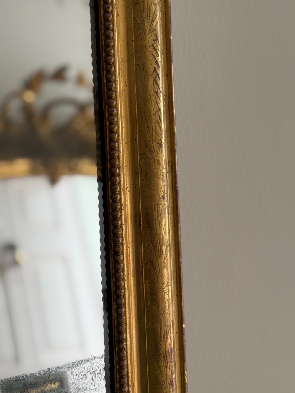 A rectangular antique French gilt mirror featuring rounded upper corners, an engraved gold leaf frame with beaded inner moulding, and foxed mercury glass. View V
