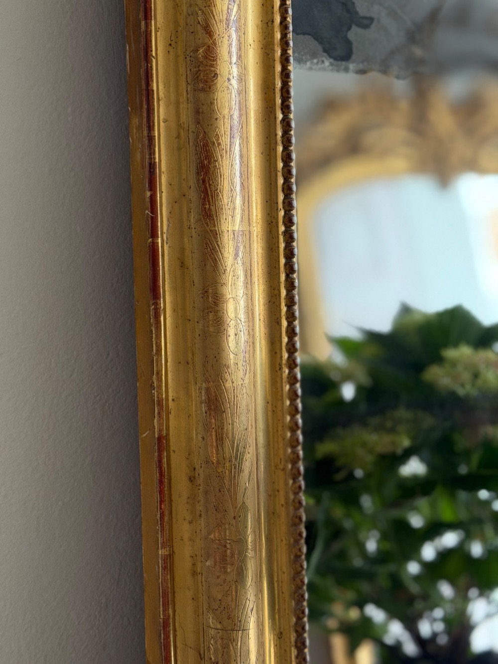 A rectangular antique French gilt mirror featuring rounded upper corners, an engraved gold leaf frame with beaded inner moulding, and foxed mercury glass. View VII