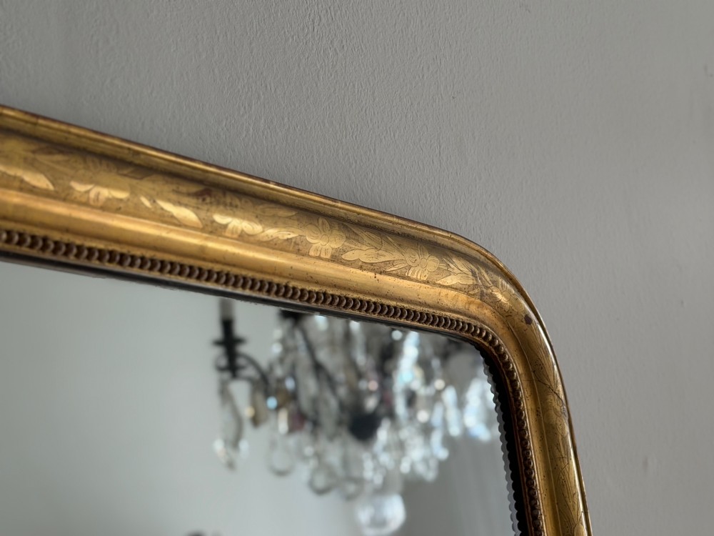 A rectangular antique French gilt mirror featuring rounded upper corners, an engraved gold leaf frame with beaded inner moulding, and foxed mercury glass. View IX