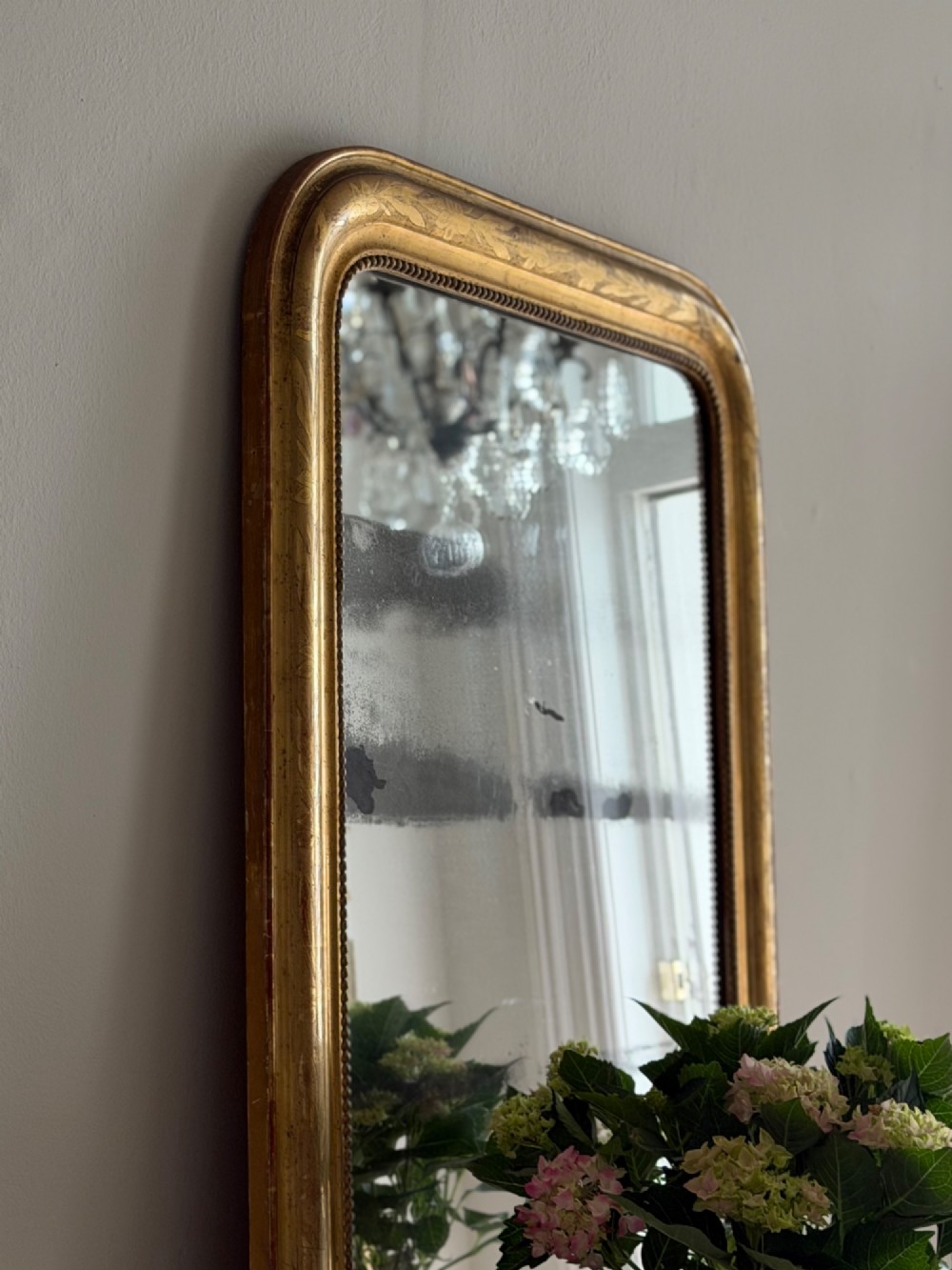A rectangular antique French gilt mirror featuring rounded upper corners, an engraved gold leaf frame with beaded inner moulding, and foxed mercury glass. View X