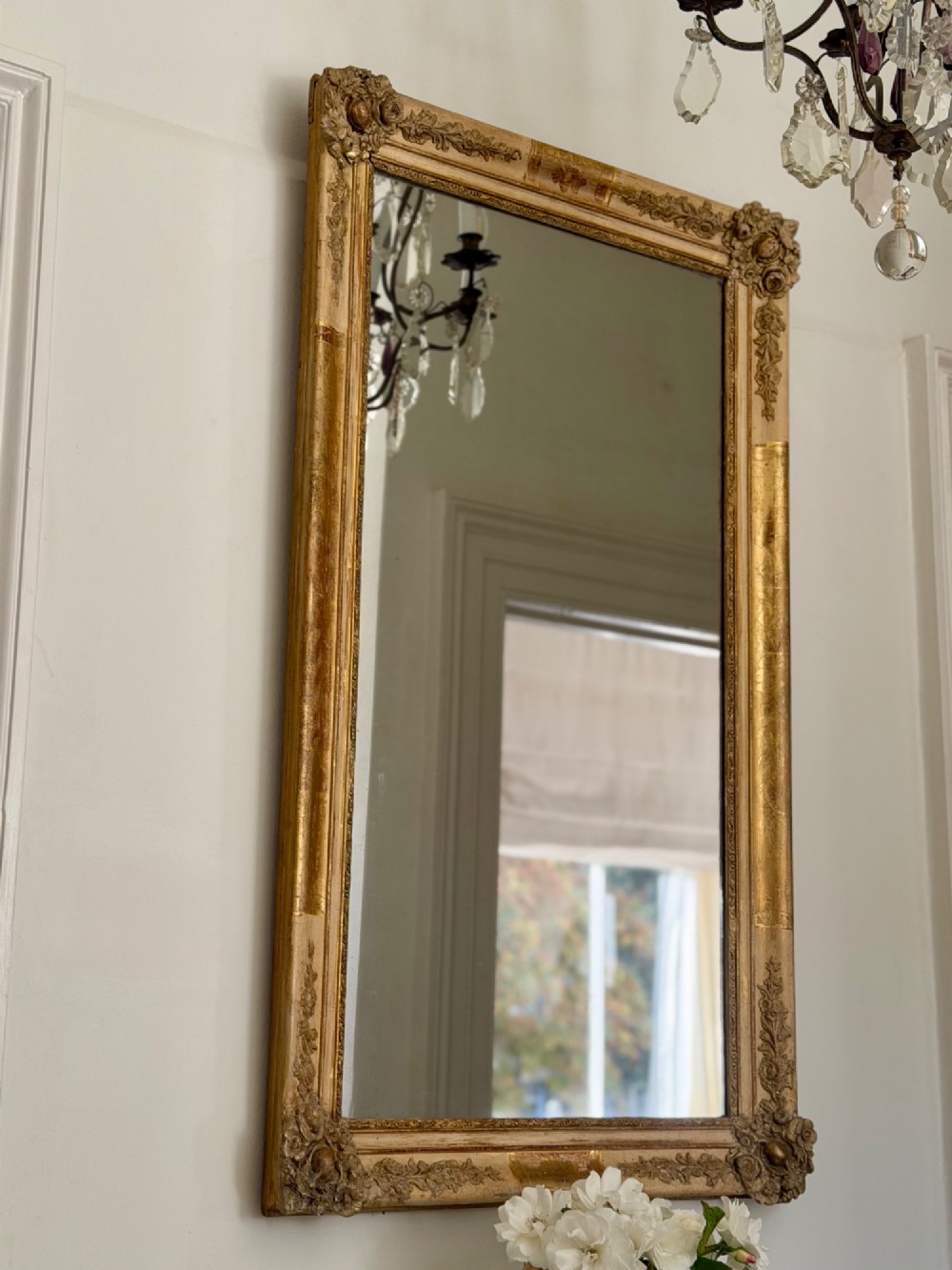 A tall rectangular nineteenth-century French Napoleon III mirror with a gilded and bare gesso frame featuring floral corner mouldings and a mercury glass plate.