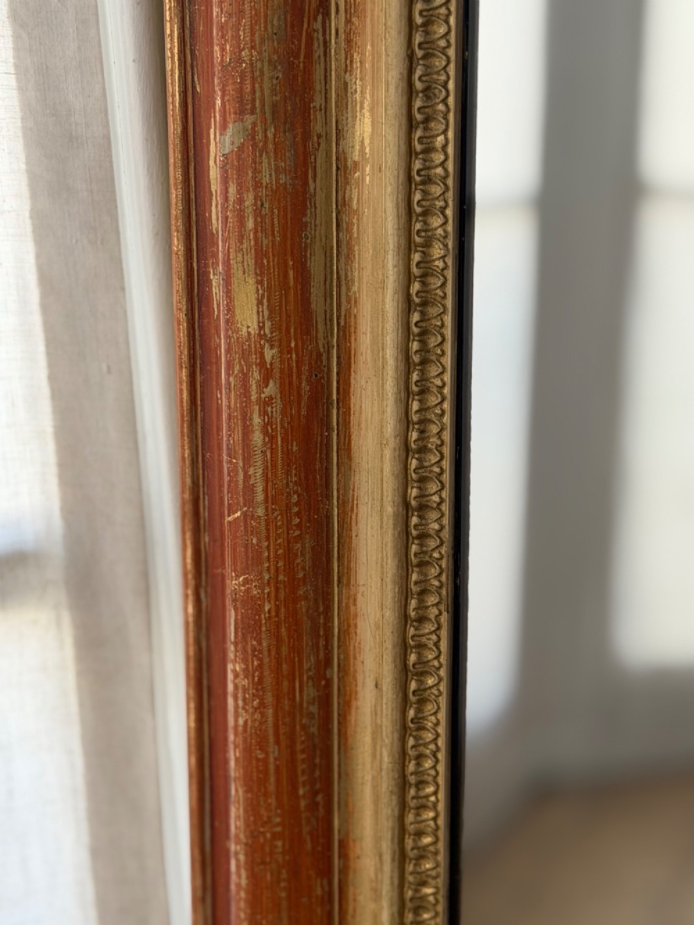 A French Louis Philippe mirror featuring a rounded-top frame with worn gold leaf finish exposing the red clay bole beneath, holding a mercury glass plate. View V
