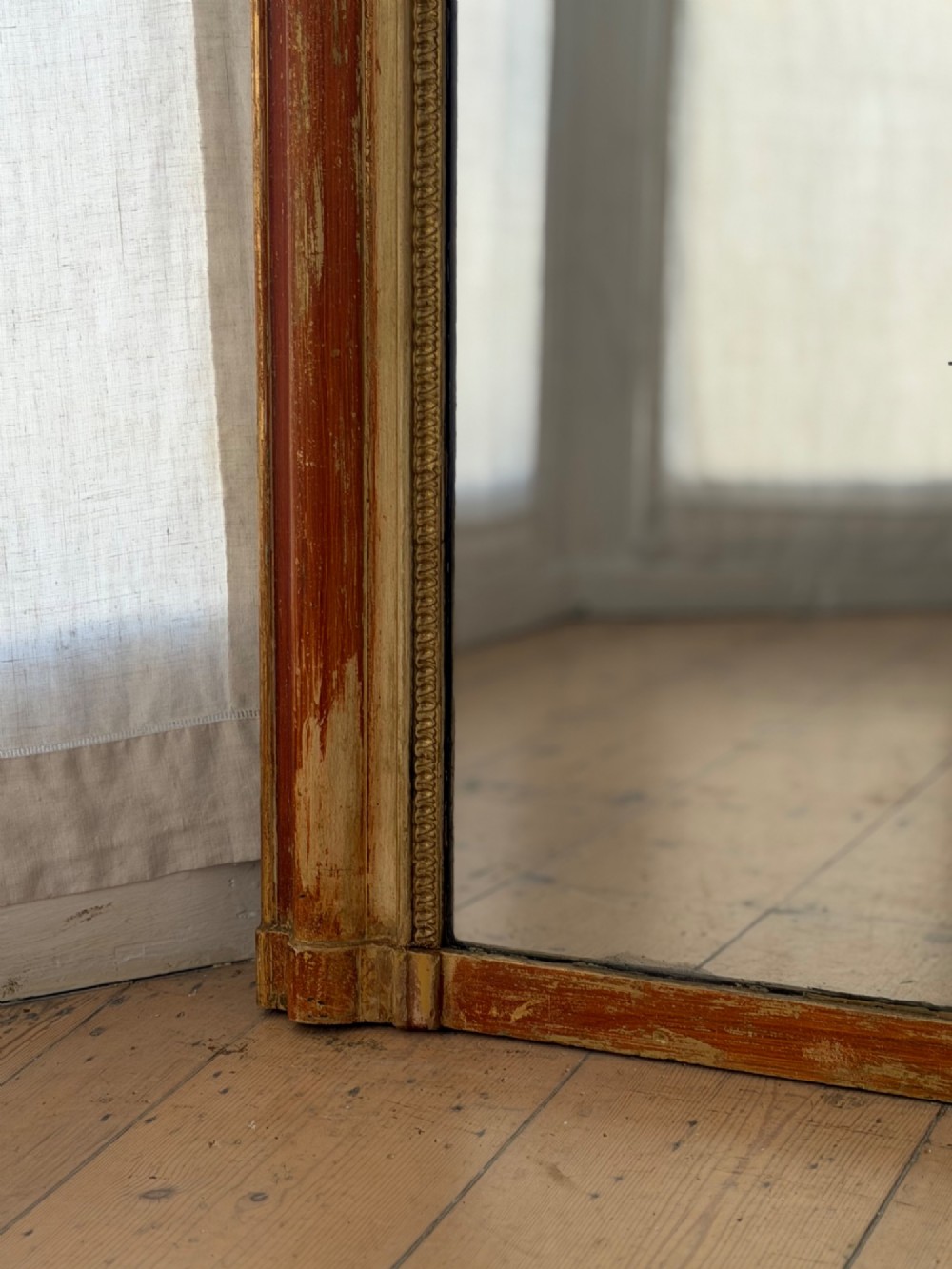 A French Louis Philippe mirror featuring a rounded-top frame with worn gold leaf finish exposing the red clay bole beneath, holding a mercury glass plate. View VII
