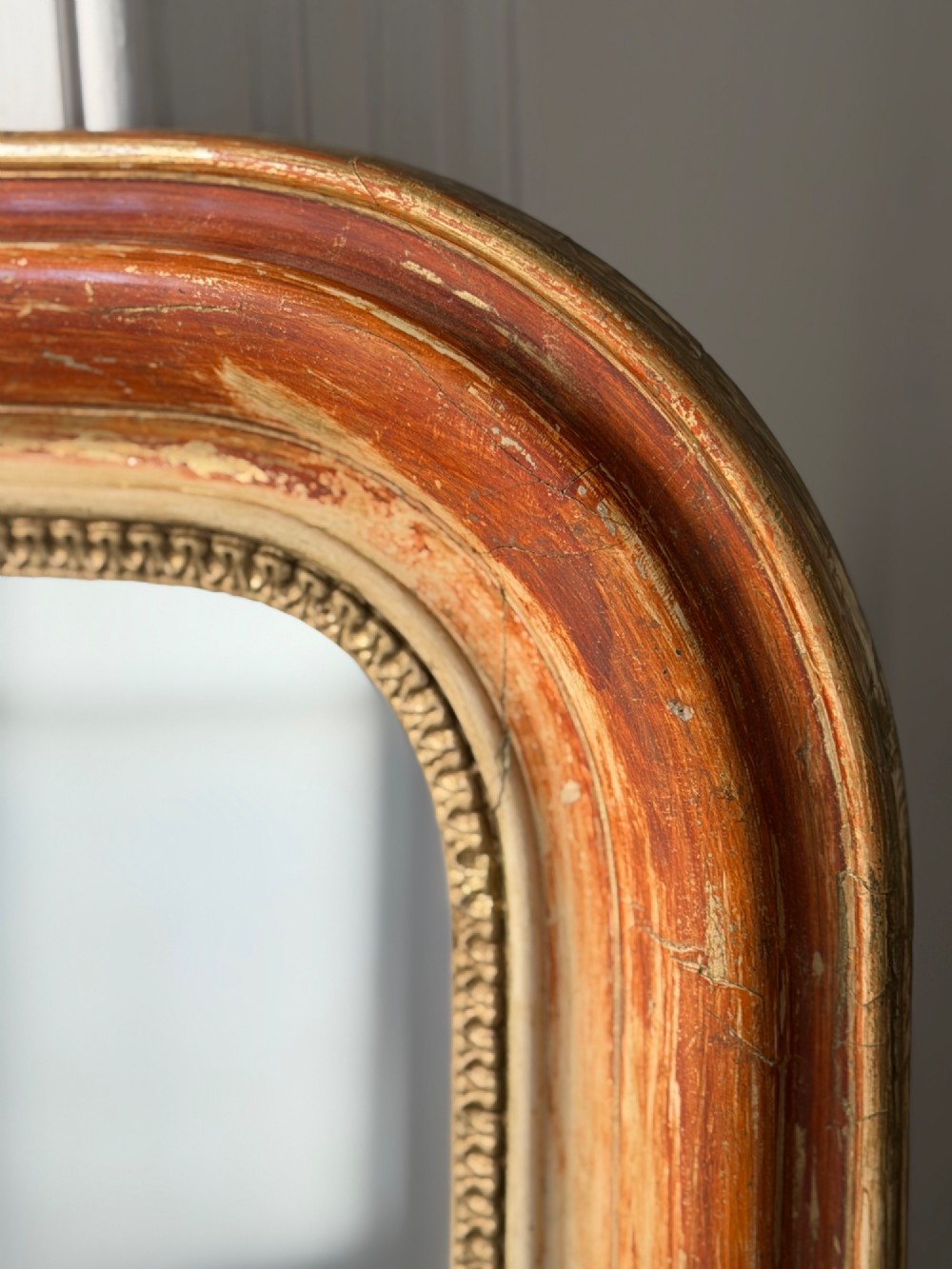 A French Louis Philippe mirror featuring a rounded-top frame with worn gold leaf finish exposing the red clay bole beneath, holding a mercury glass plate. View VIII