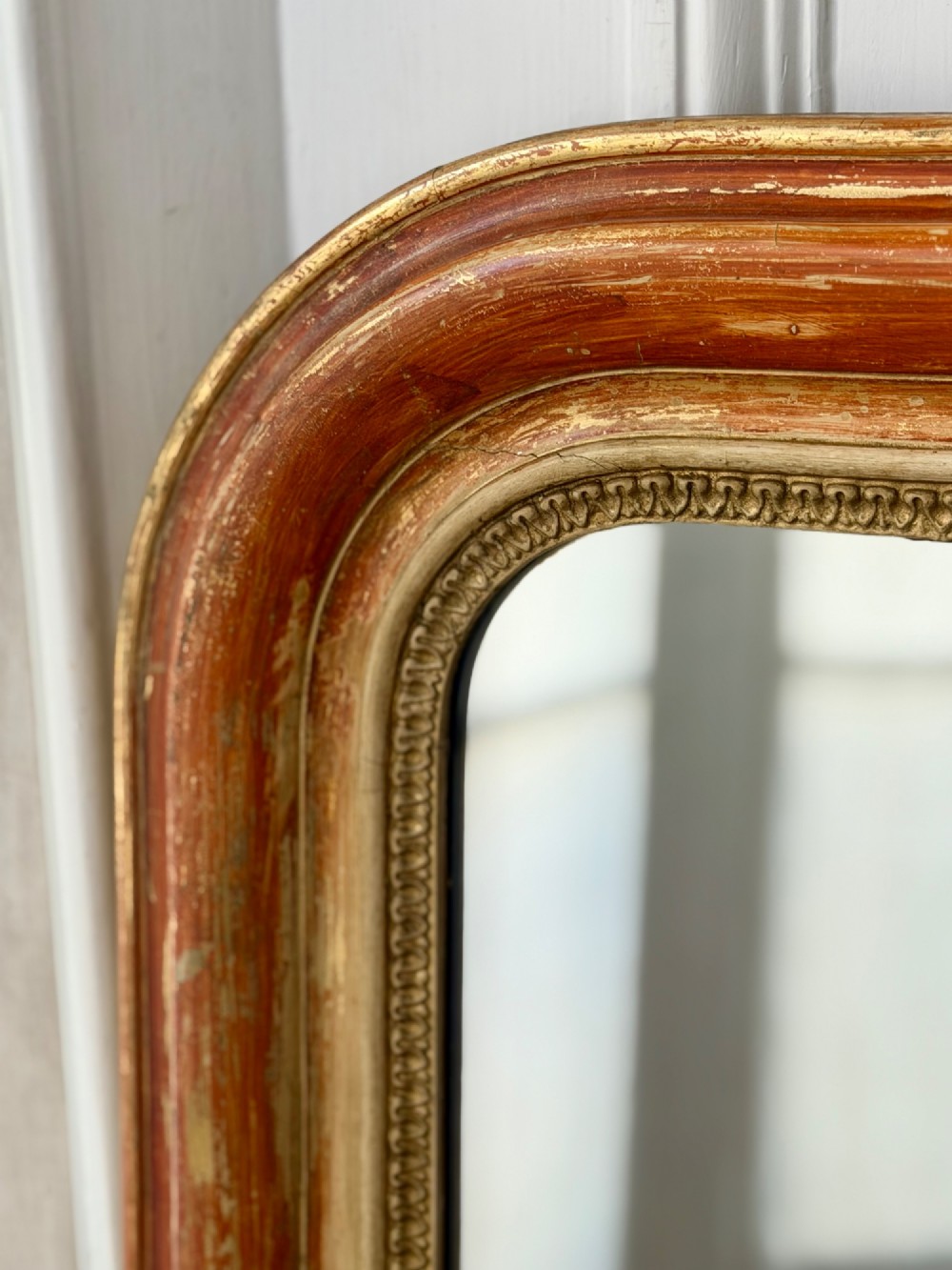 A French Louis Philippe mirror featuring a rounded-top frame with worn gold leaf finish exposing the red clay bole beneath, holding a mercury glass plate. View IX