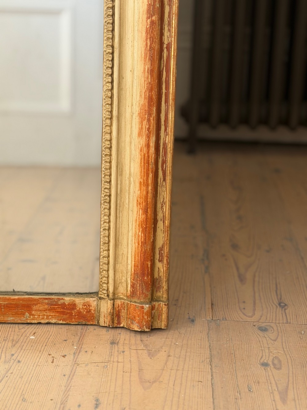 A French Louis Philippe mirror featuring a rounded-top frame with worn gold leaf finish exposing the red clay bole beneath, holding a mercury glass plate. View X