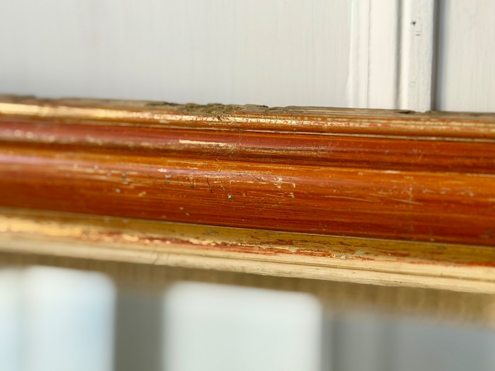 A French Louis Philippe mirror featuring a rounded-top frame with worn gold leaf finish exposing the red clay bole beneath, holding a mercury glass plate. View XI