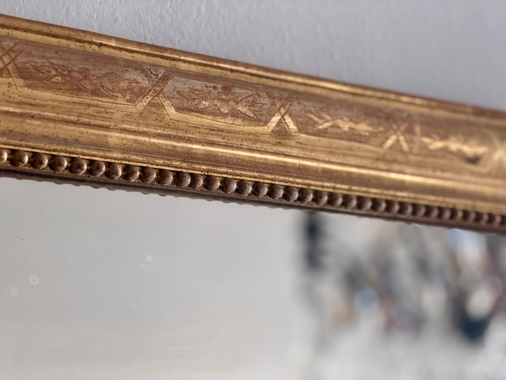 A rectangular 19th-century Louis Philippe mirror featuring rounded upper corners, an engraved gold leaf frame, beaded interior trim, and aged mirror glass. View IX