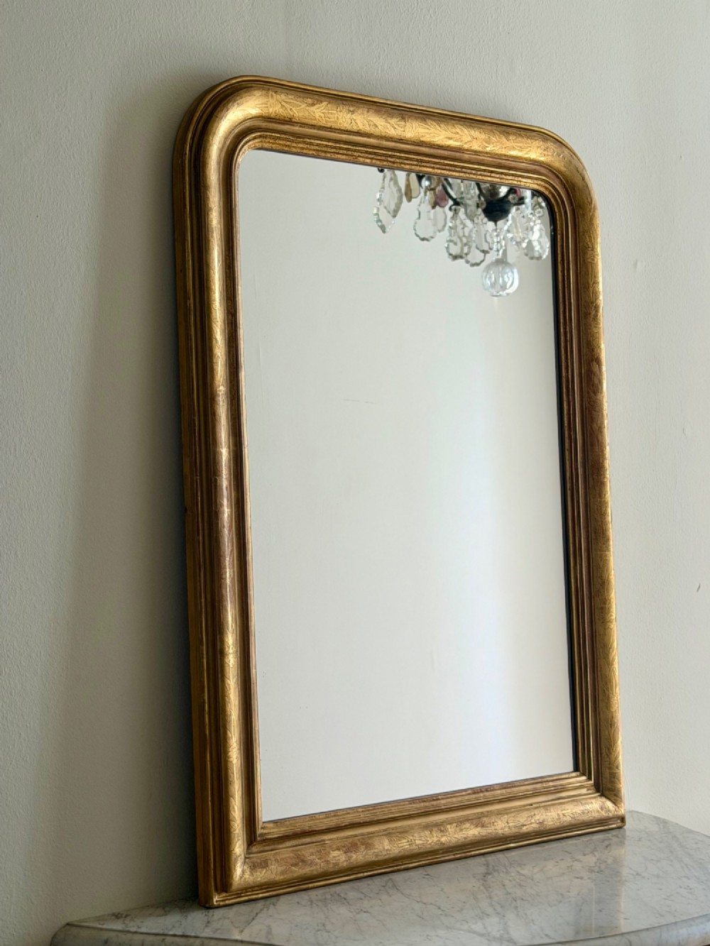 An antique French Louis Philippe wall mirror featuring a rectangular gilded frame with rounded upper corners, subtle etched foliate patterns, and a mercury glass plate.