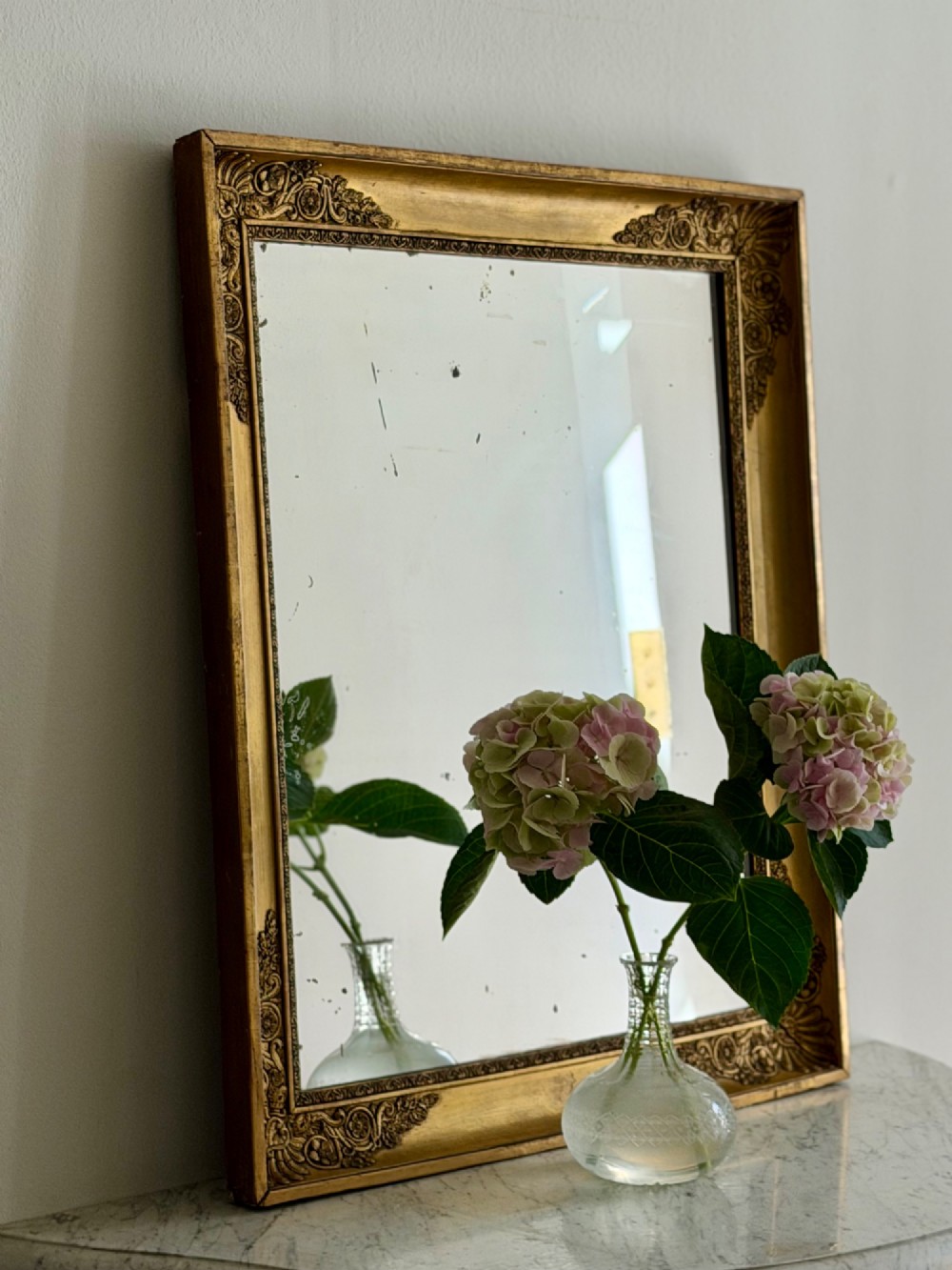 A rectangular antique French giltwood mirror featuring carved corner spandrels and a foxed glass plate. View II