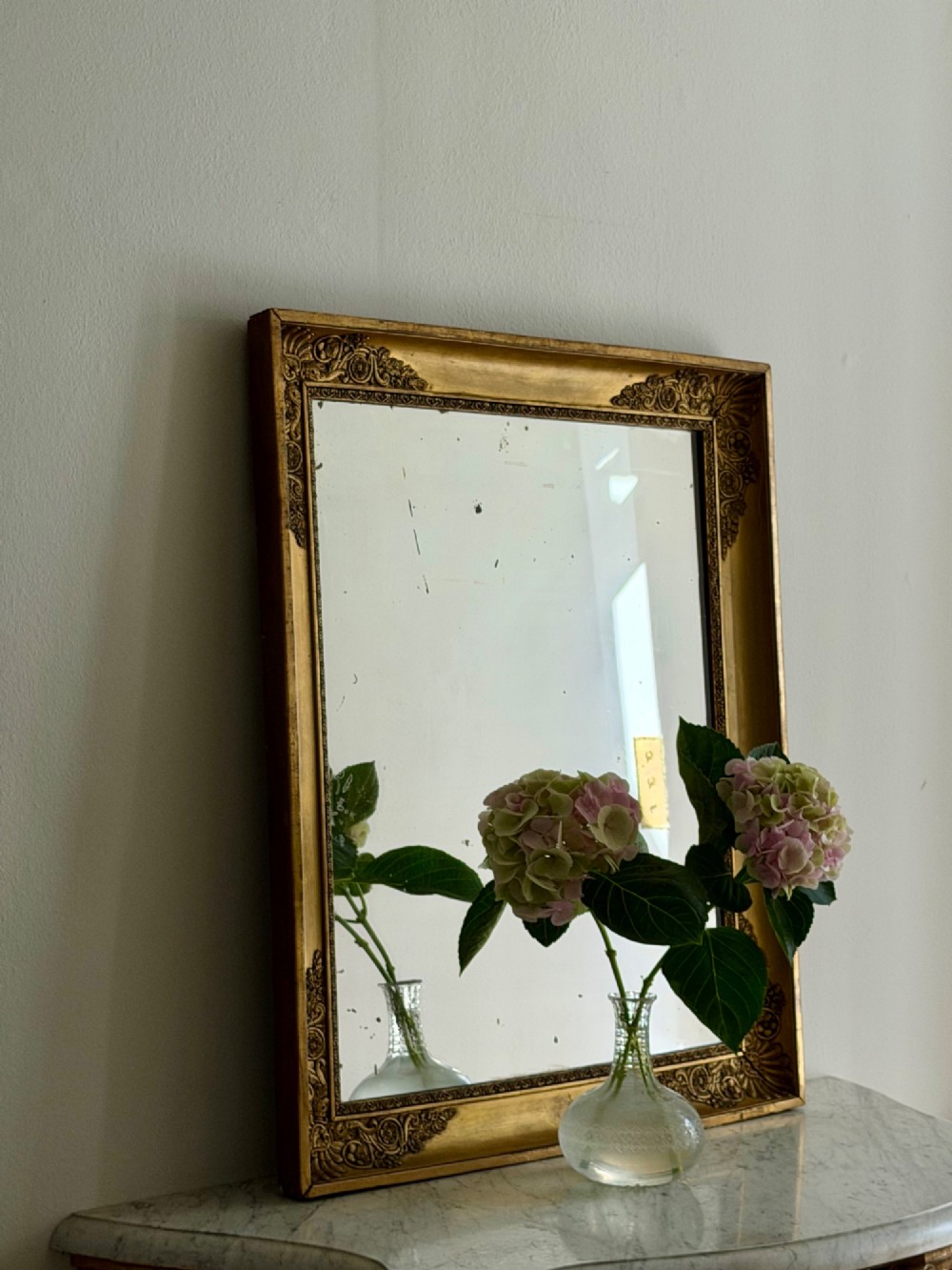 A rectangular antique French giltwood mirror featuring carved corner spandrels and a foxed glass plate. View III
