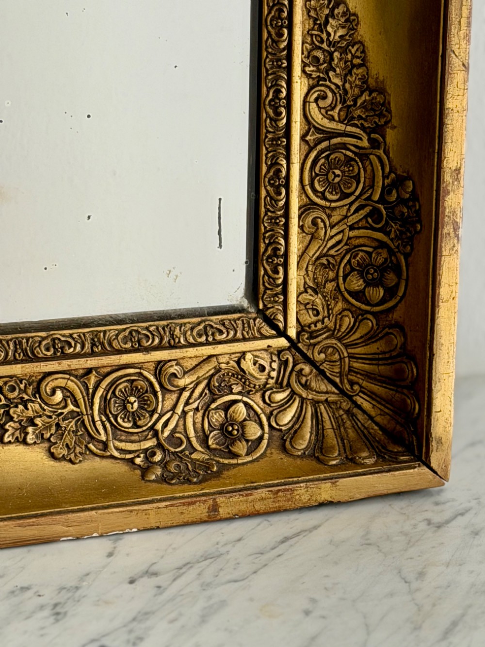 A rectangular antique French giltwood mirror featuring carved corner spandrels and a foxed glass plate. View VI