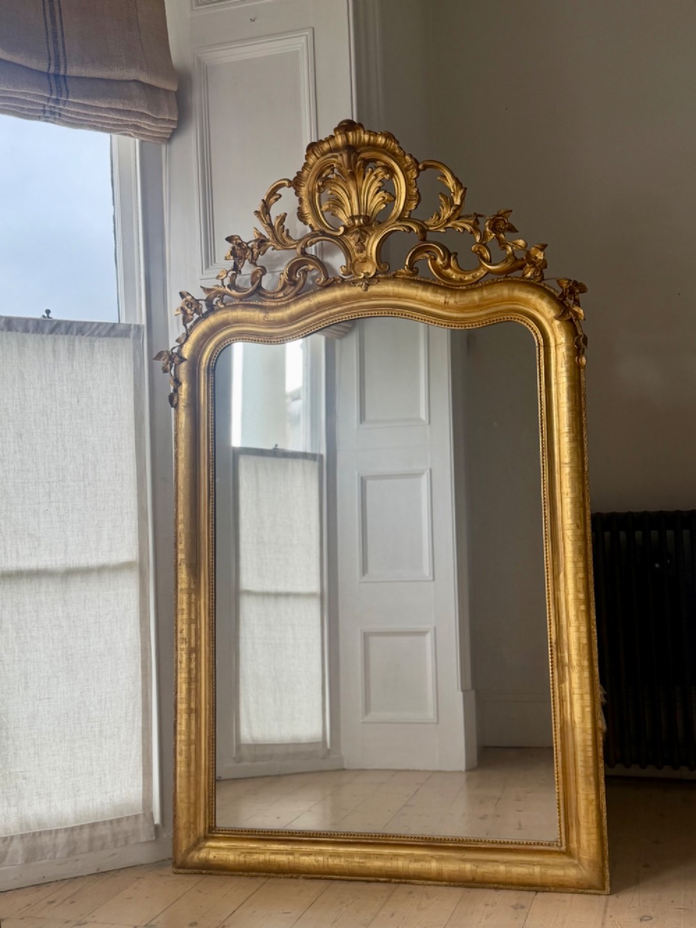 A large French Louis XV style giltwood mirror featuring an ornate rocaille cresting, foliate scrolls, and mercury glass mirror plate.