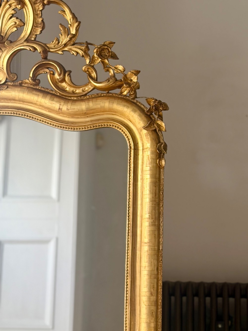 A large French Louis XV style giltwood mirror featuring an ornate rocaille cresting, foliate scrolls, and mercury glass mirror plate. View II