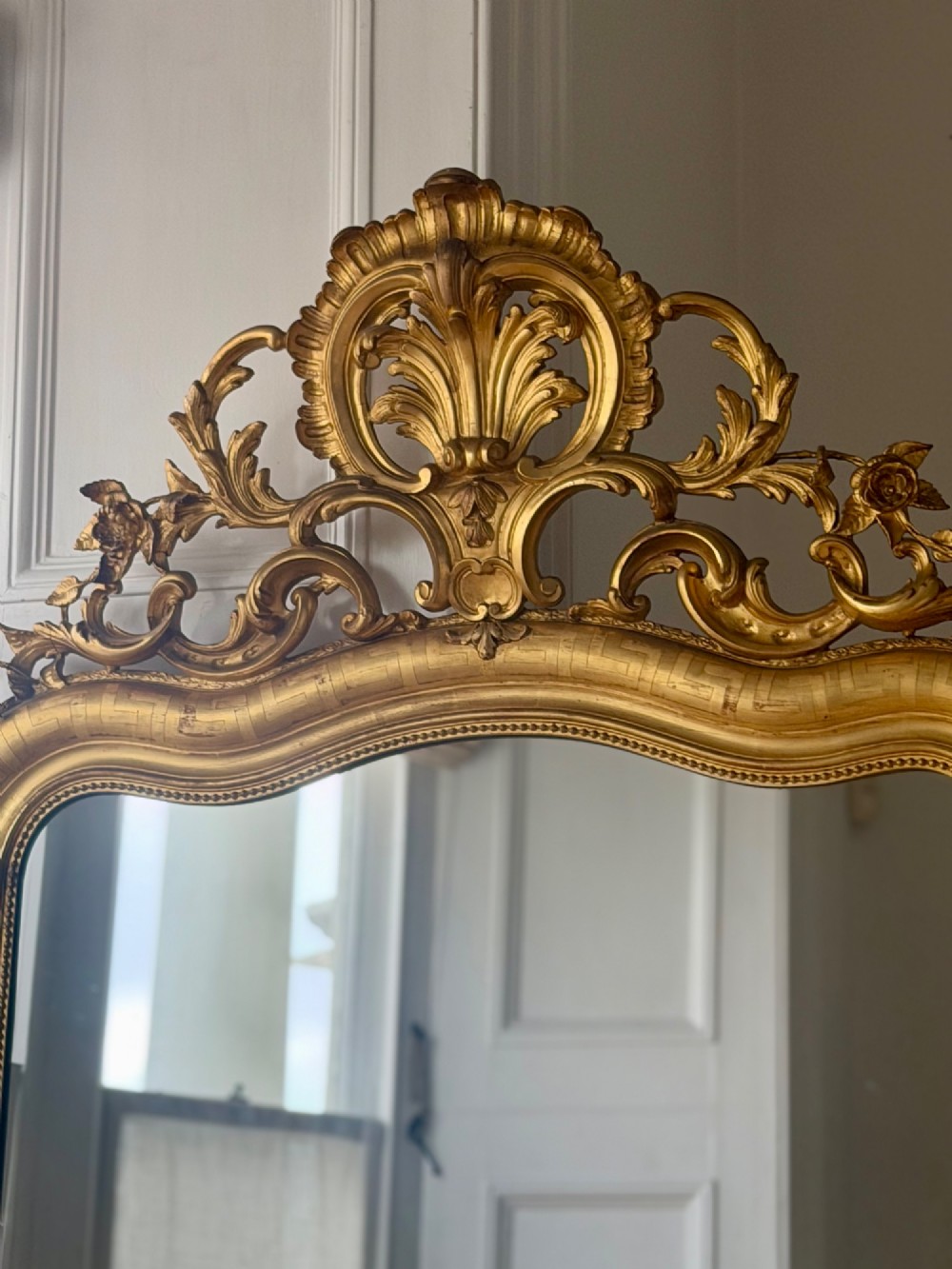 A large French Louis XV style giltwood mirror featuring an ornate rocaille cresting, foliate scrolls, and mercury glass mirror plate. View III