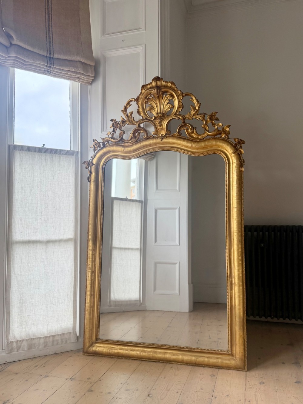 A large French Louis XV style giltwood mirror featuring an ornate rocaille cresting, foliate scrolls, and mercury glass mirror plate. View VI