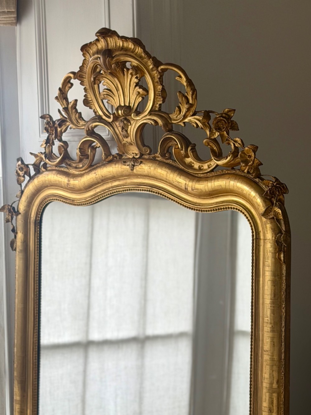 A large French Louis XV style giltwood mirror featuring an ornate rocaille cresting, foliate scrolls, and mercury glass mirror plate. View VII