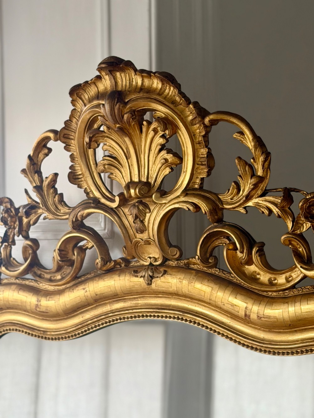 A large French Louis XV style giltwood mirror featuring an ornate rocaille cresting, foliate scrolls, and mercury glass mirror plate. View IX