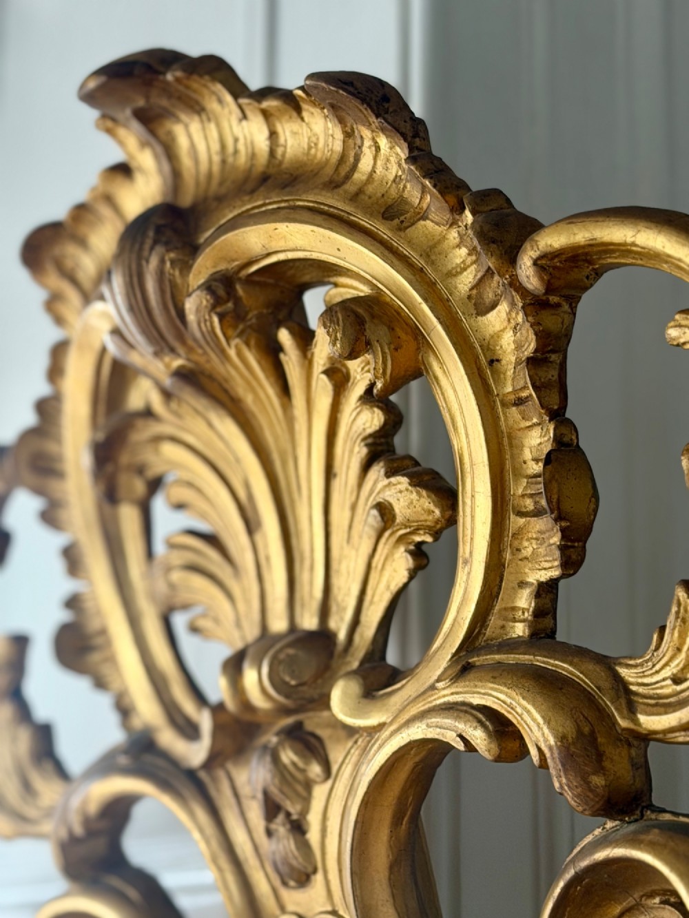 A large French Louis XV style giltwood mirror featuring an ornate rocaille cresting, foliate scrolls, and mercury glass mirror plate. View X