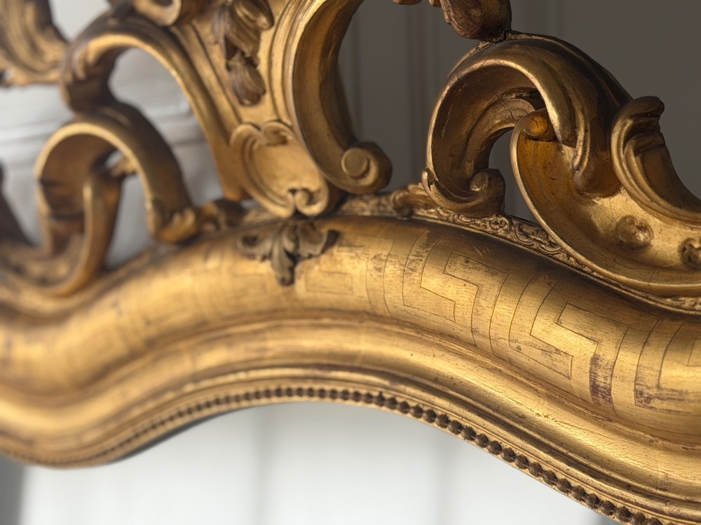 A large French Louis XV style giltwood mirror featuring an ornate rocaille cresting, foliate scrolls, and mercury glass mirror plate. View XII