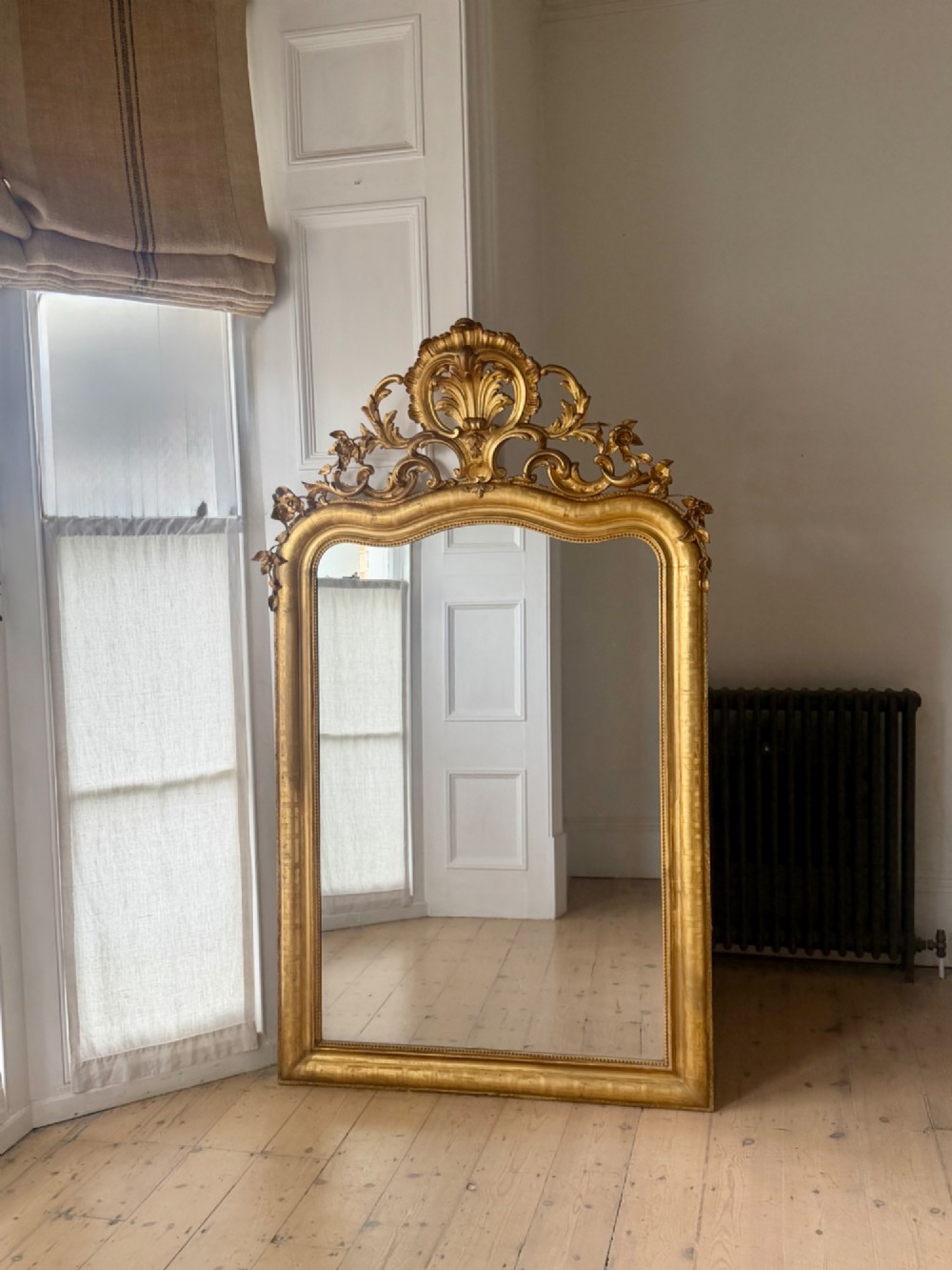 A large French Louis XV style giltwood mirror featuring an ornate rocaille cresting, foliate scrolls, and mercury glass mirror plate. View XIII