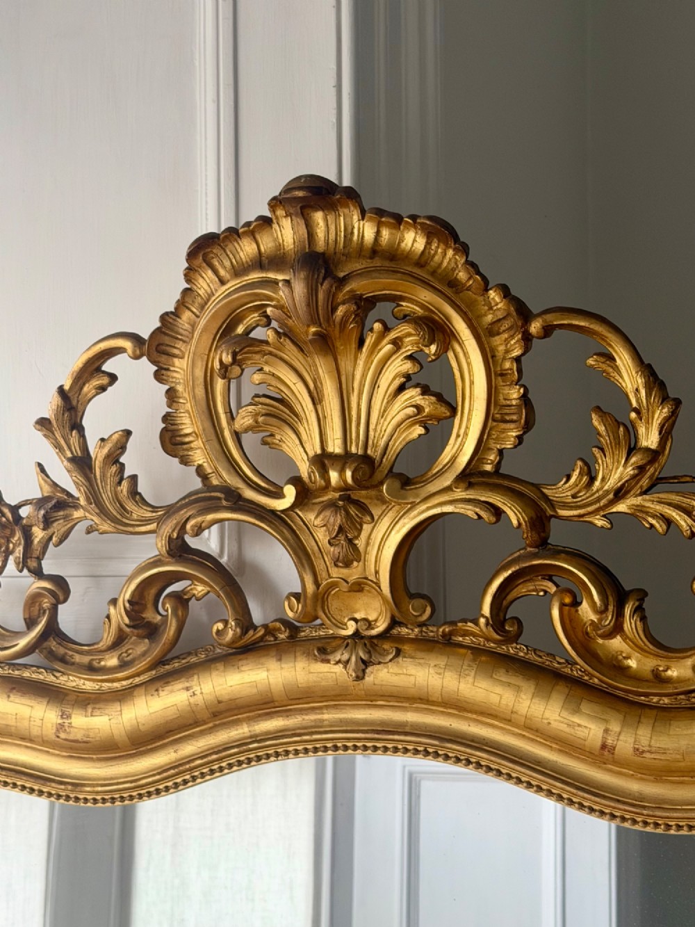 A large French Louis XV style giltwood mirror featuring an ornate rocaille cresting, foliate scrolls, and mercury glass mirror plate. View XV