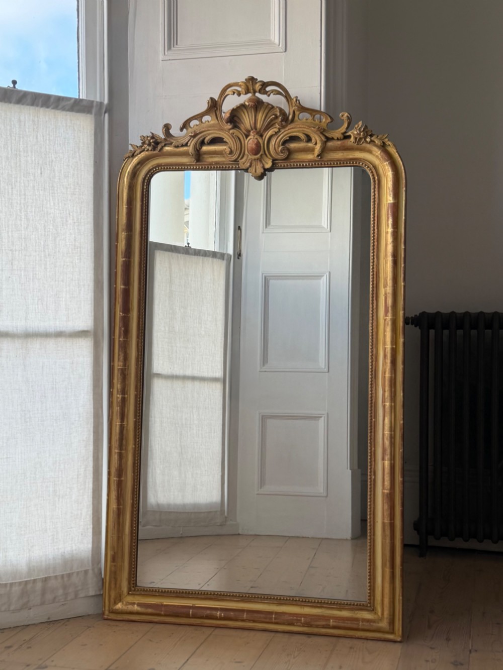 A tall rectangular French Louis Philippe wall mirror with rounded top corners, an elaborate carved shell cresting, a gold gilt frame over red gesso, and a beaded inner trim.