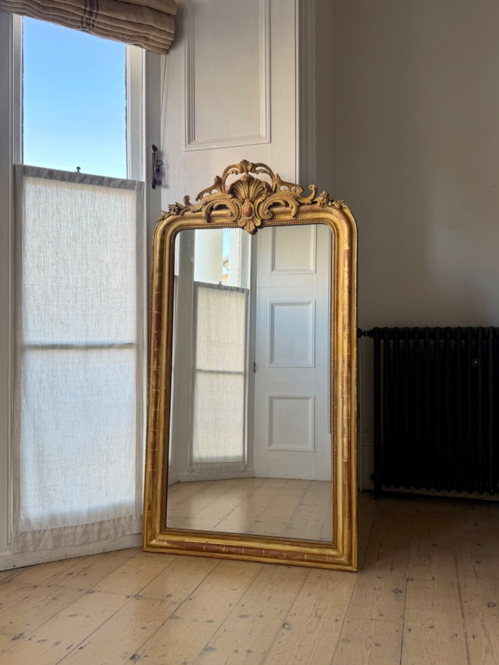 A tall rectangular French Louis Philippe wall mirror with rounded top corners, an elaborate carved shell cresting, a gold gilt frame over red gesso, and a beaded inner trim. View IV