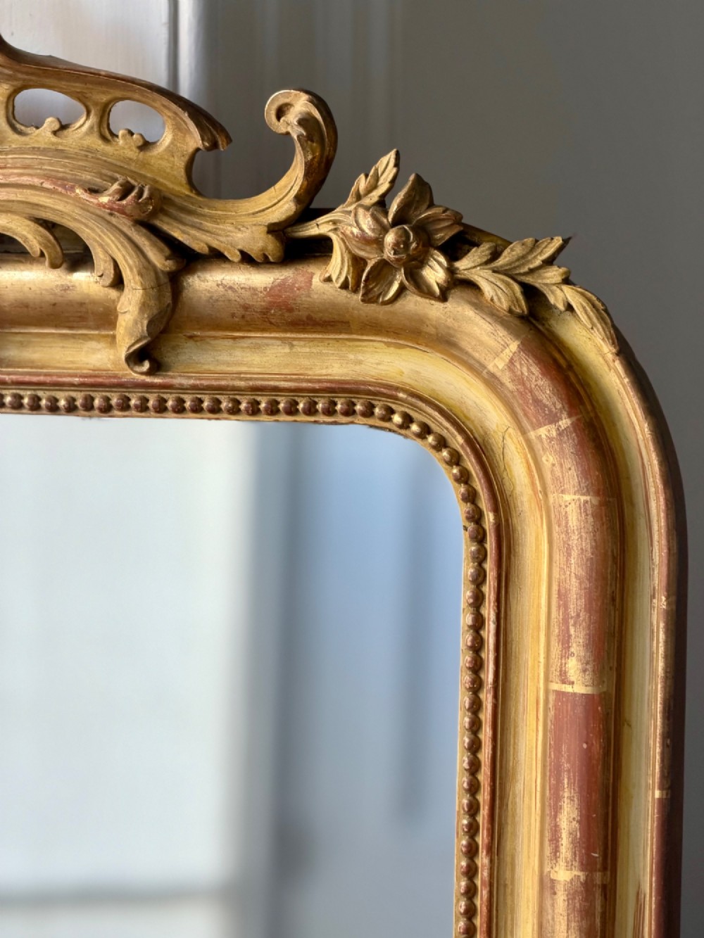 A tall rectangular French Louis Philippe wall mirror with rounded top corners, an elaborate carved shell cresting, a gold gilt frame over red gesso, and a beaded inner trim. View V