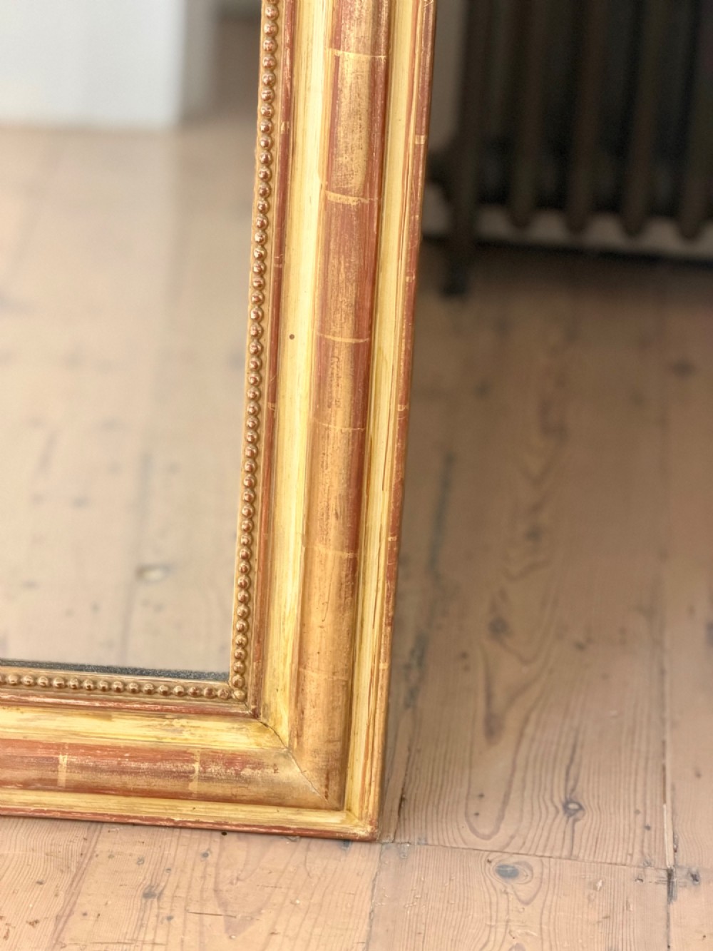 A tall rectangular French Louis Philippe wall mirror with rounded top corners, an elaborate carved shell cresting, a gold gilt frame over red gesso, and a beaded inner trim. View VI
