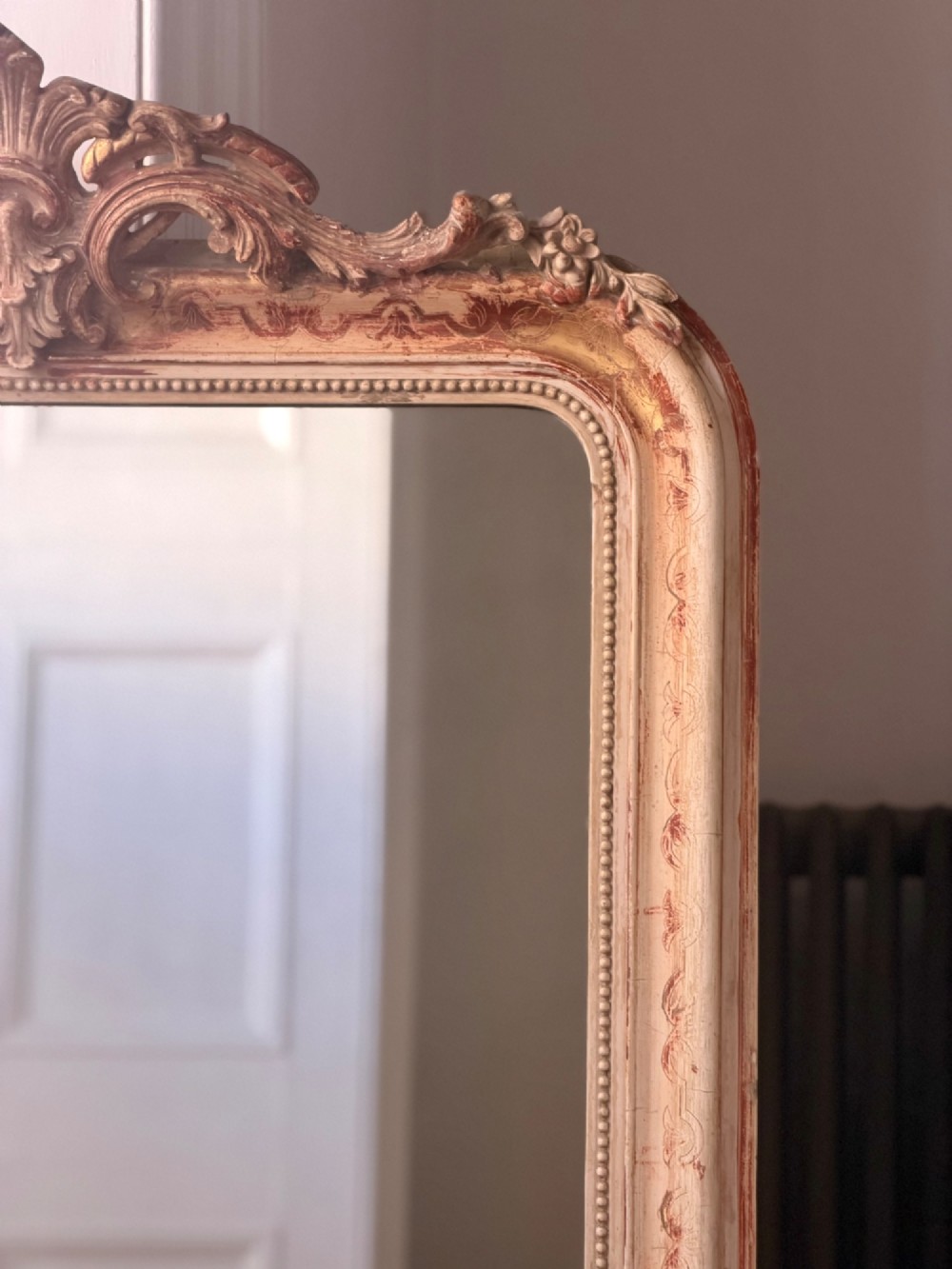 An antique French mirror featuring an arched top frame with a carved cresting and distressed off-white gesso finish. View II