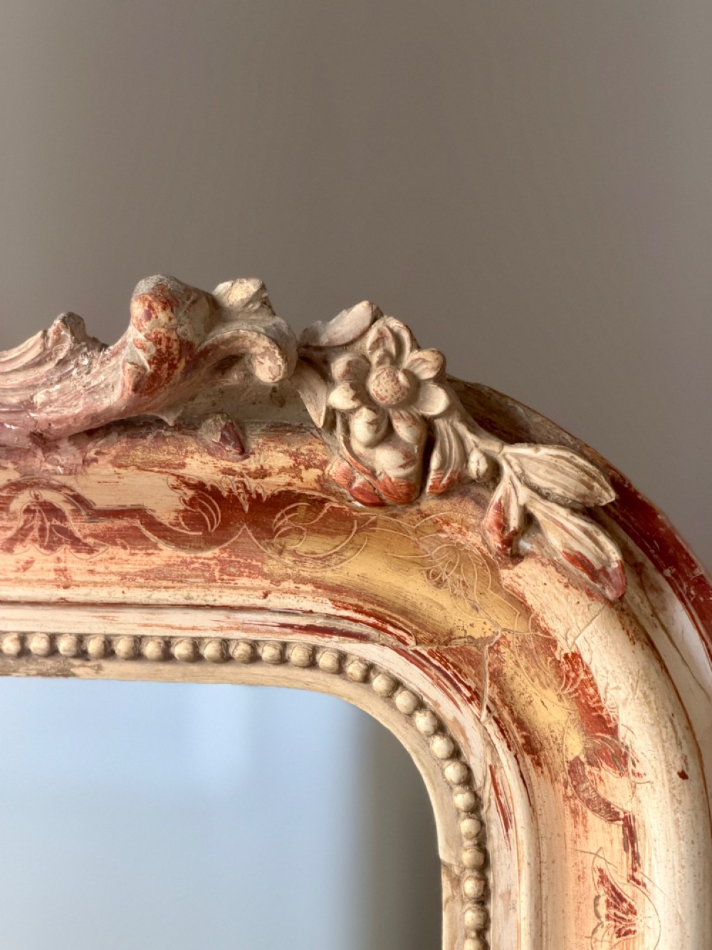 An antique French mirror featuring an arched top frame with a carved cresting and distressed off-white gesso finish. View III