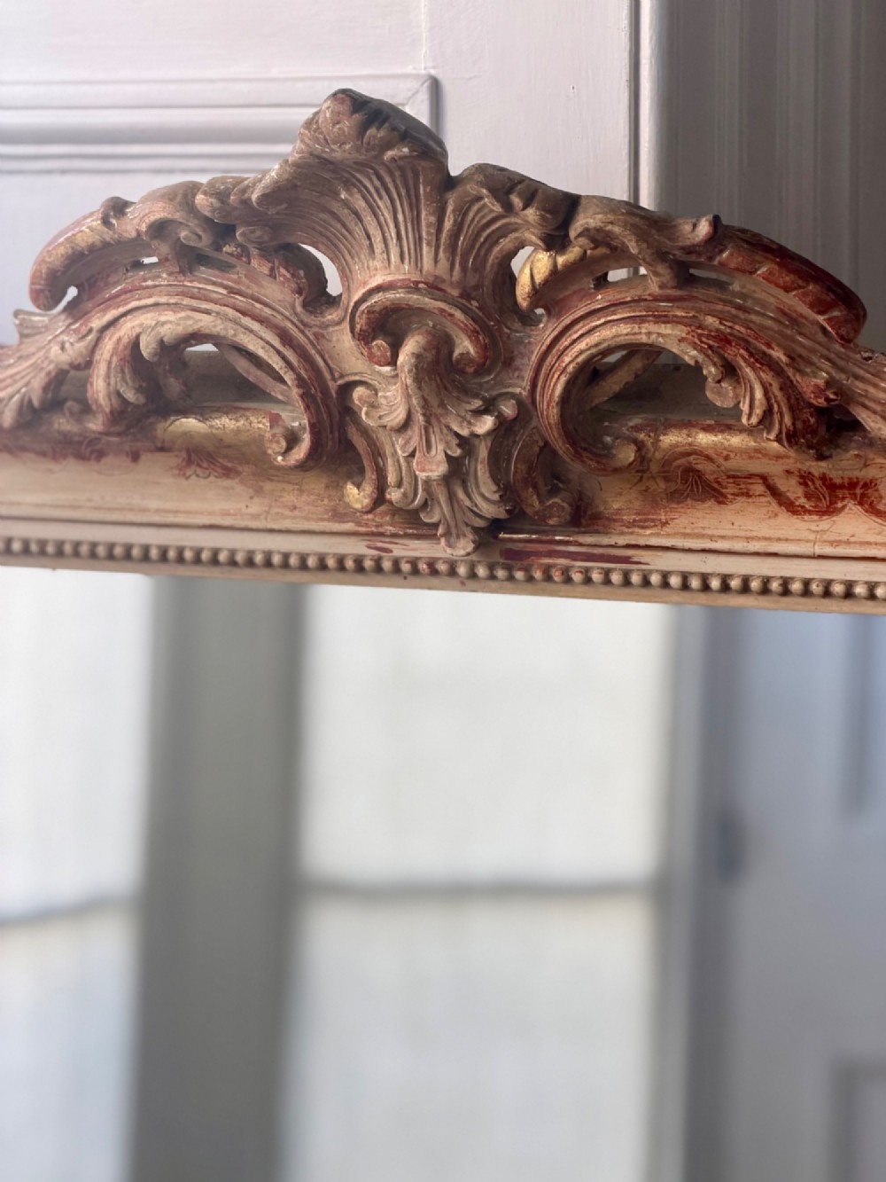 An antique French mirror featuring an arched top frame with a carved cresting and distressed off-white gesso finish. View IV