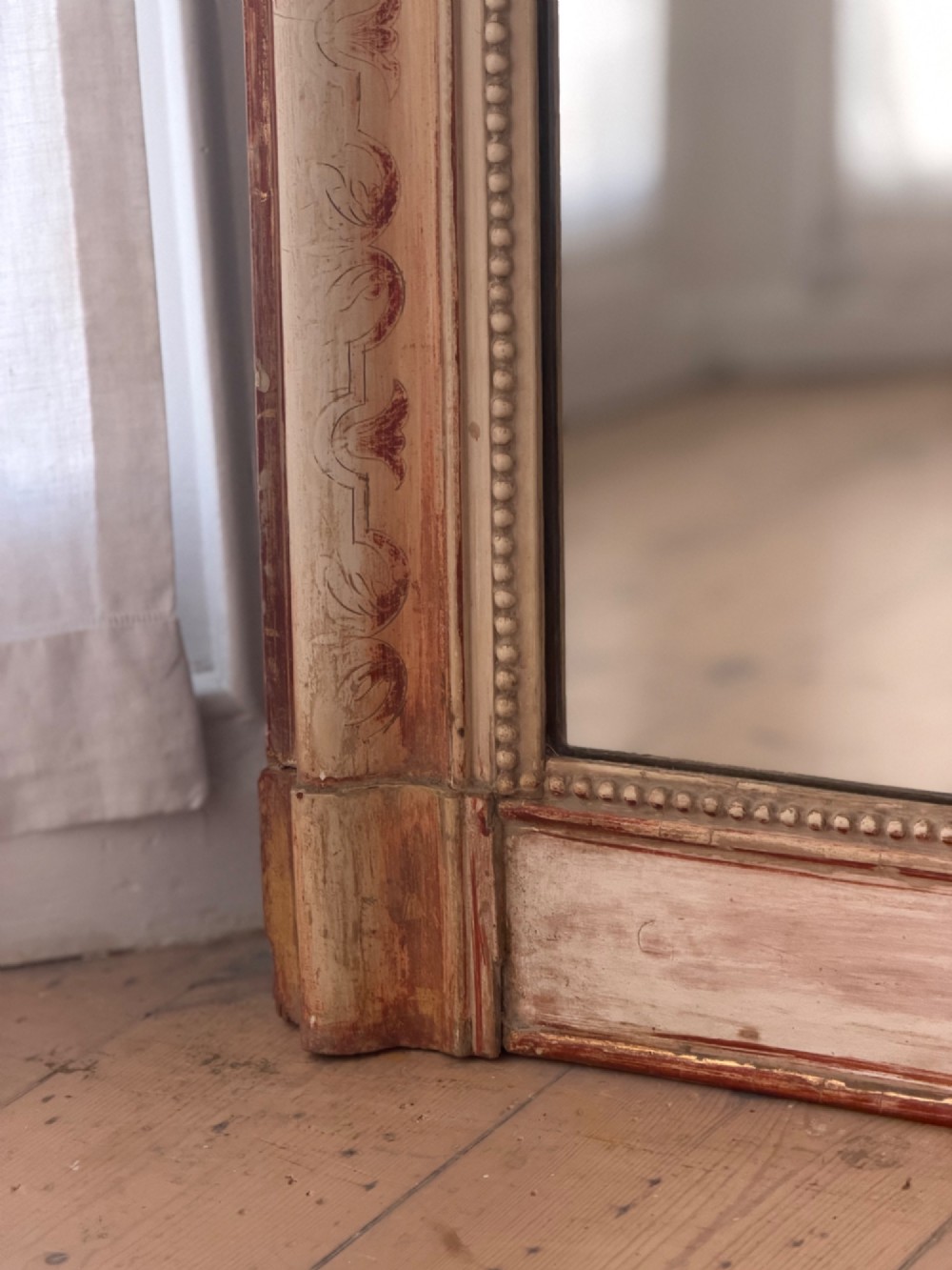 An antique French mirror featuring an arched top frame with a carved cresting and distressed off-white gesso finish. View VI