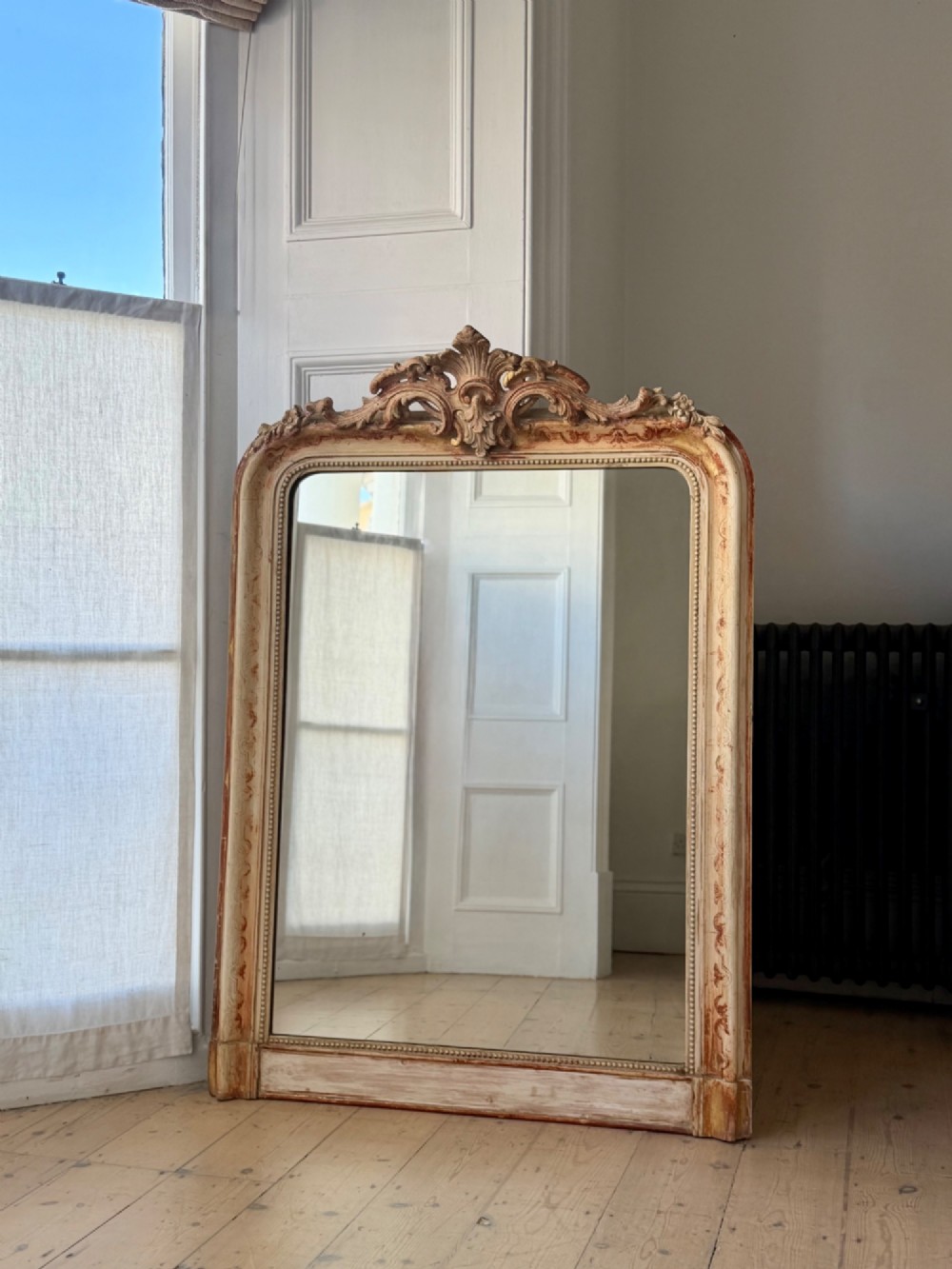 An antique French mirror featuring an arched top frame with a carved cresting and distressed off-white gesso finish. View XI