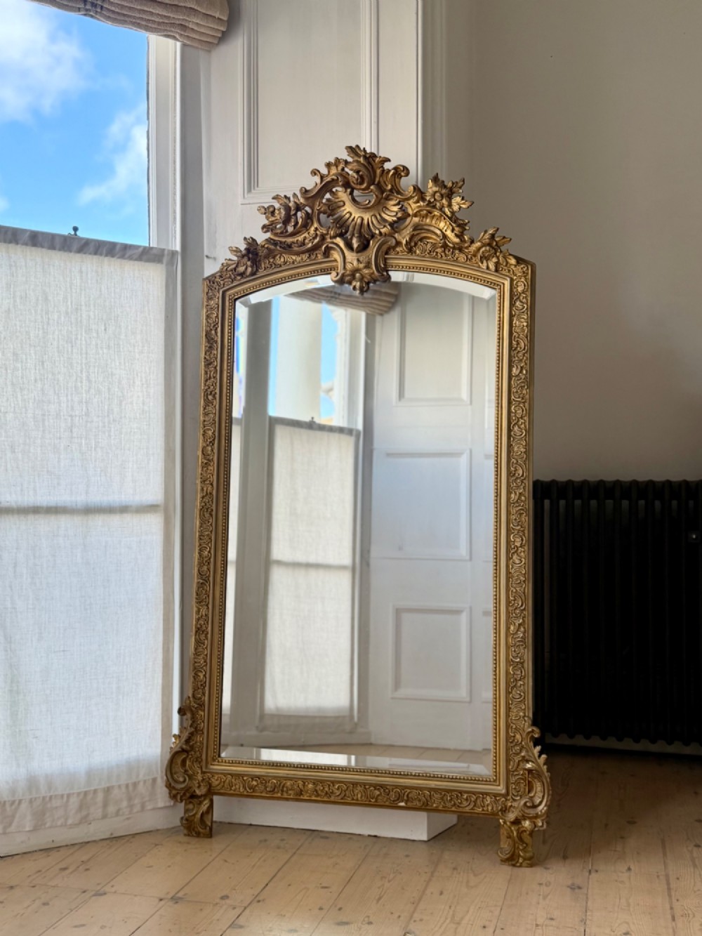A large French gilded wood frame mirror featuring an arched top, a carved scroll cresting, and bevelled edge glass.