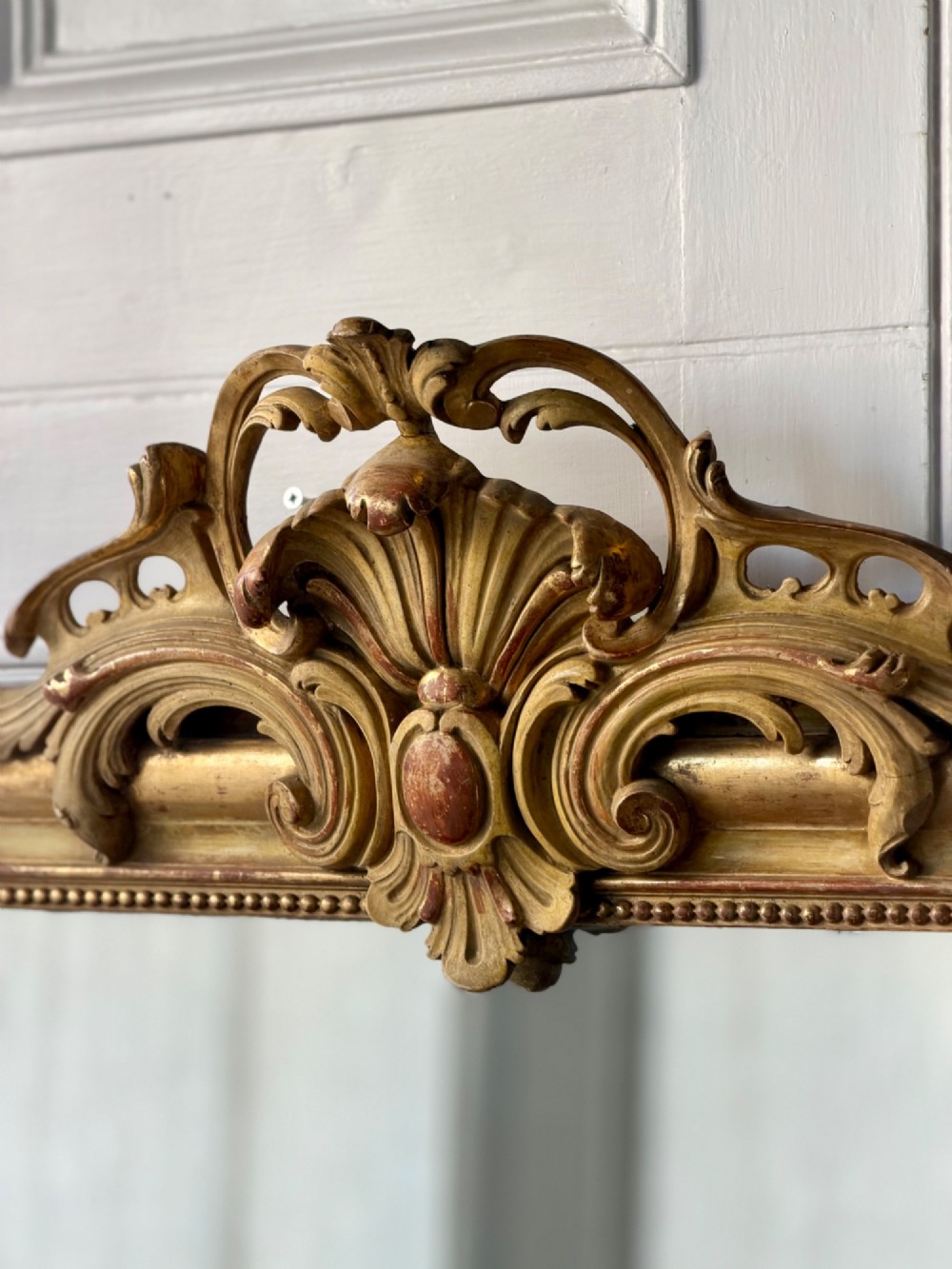 A tall rectangular French Louis Philippe wall mirror with rounded top corners, an elaborate carved shell cresting, a gold gilt frame over red gesso, and a beaded inner trim. View XI