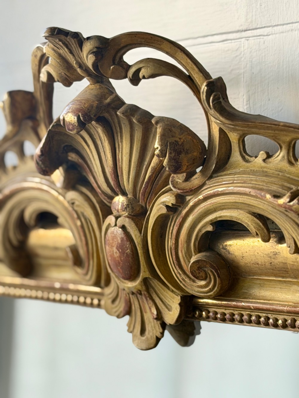 A tall rectangular French Louis Philippe wall mirror with rounded top corners, an elaborate carved shell cresting, a gold gilt frame over red gesso, and a beaded inner trim. View XII
