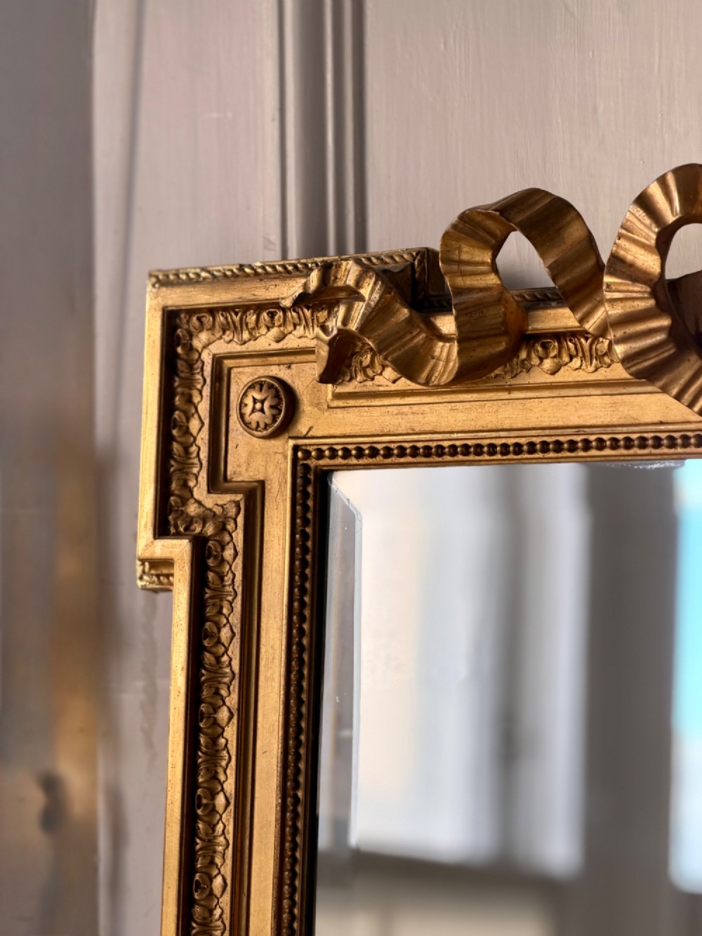 A tall rectangular gold giltwood full-length mirror featuring a carved bow ribbon cresting, beaded inner frame, and bevelled glass plate. View IV