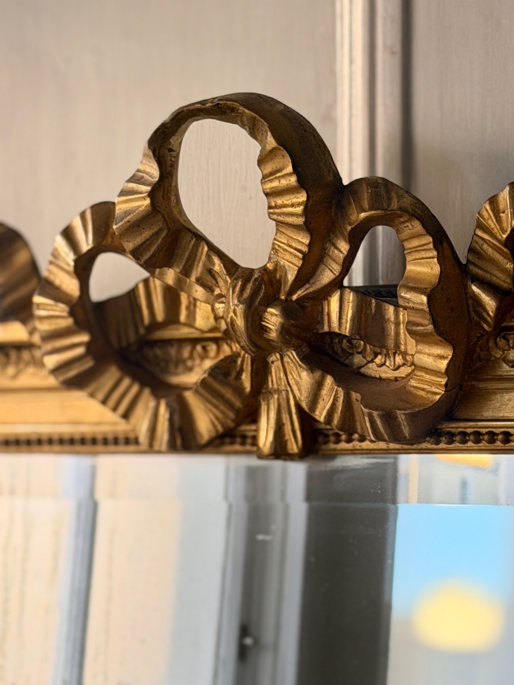 A tall rectangular gold giltwood full-length mirror featuring a carved bow ribbon cresting, beaded inner frame, and bevelled glass plate. View V