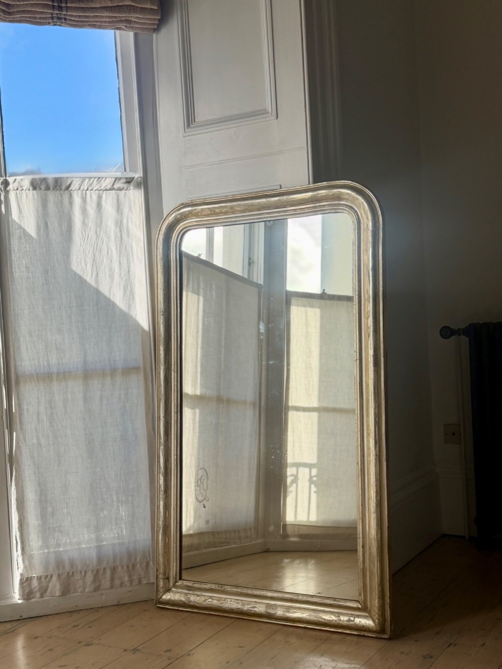 A tall rectangular antique French mirror featuring rounded top corners and a simple silver gilt frame. View VIII