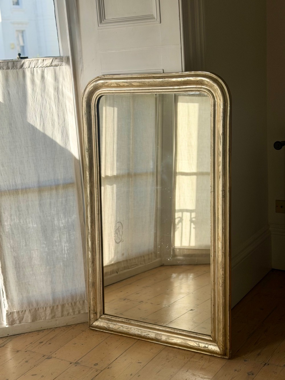 A tall rectangular antique French mirror featuring rounded top corners and a simple silver gilt frame. View X