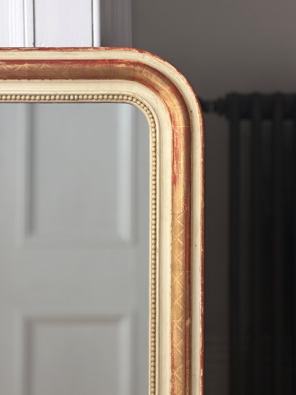 An antique French wall mirror with a rounded arched top, distressed gold leaf and cream gesso frame featuring incised geometric patterns and beaded inner edge. View II