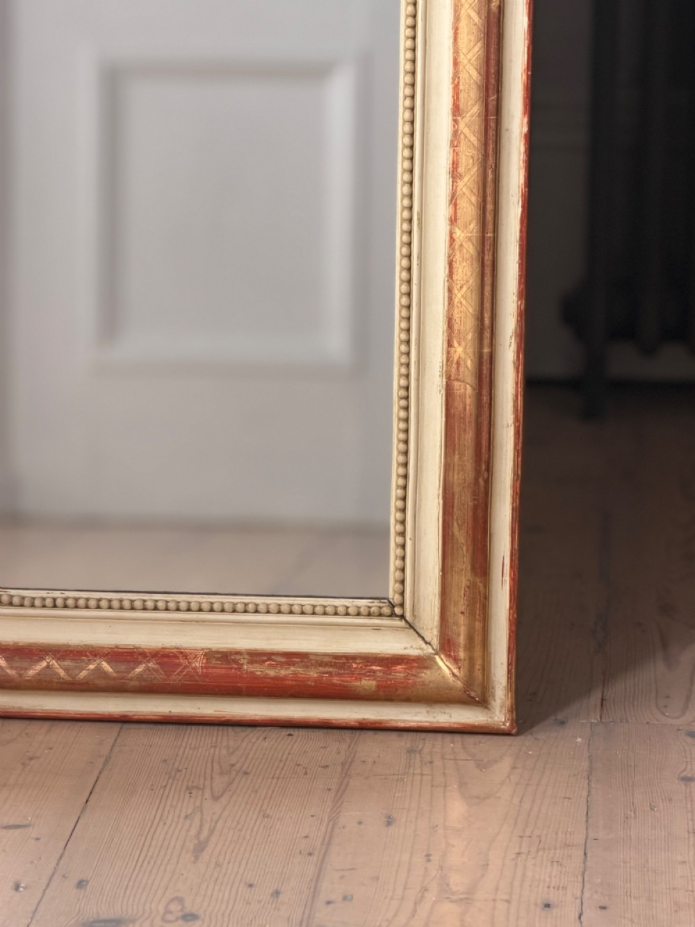 An antique French wall mirror with a rounded arched top, distressed gold leaf and cream gesso frame featuring incised geometric patterns and beaded inner edge. View III