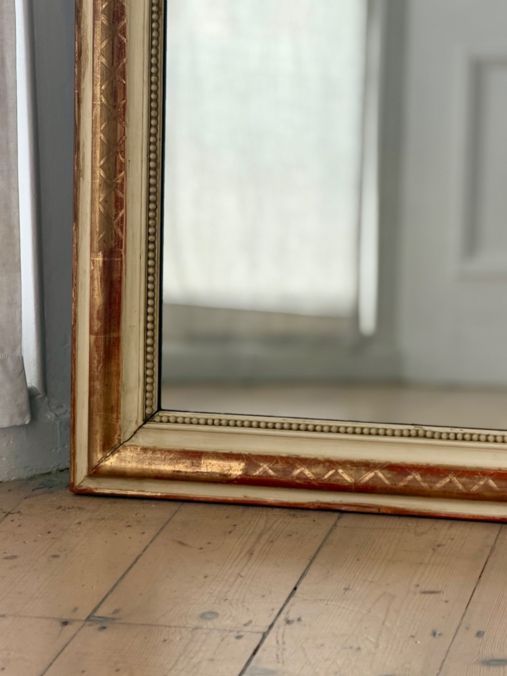 An antique French wall mirror with a rounded arched top, distressed gold leaf and cream gesso frame featuring incised geometric patterns and beaded inner edge. View IV