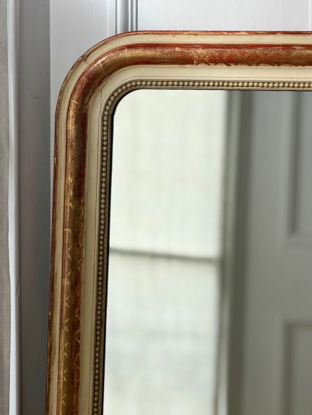 An antique French wall mirror with a rounded arched top, distressed gold leaf and cream gesso frame featuring incised geometric patterns and beaded inner edge. View V