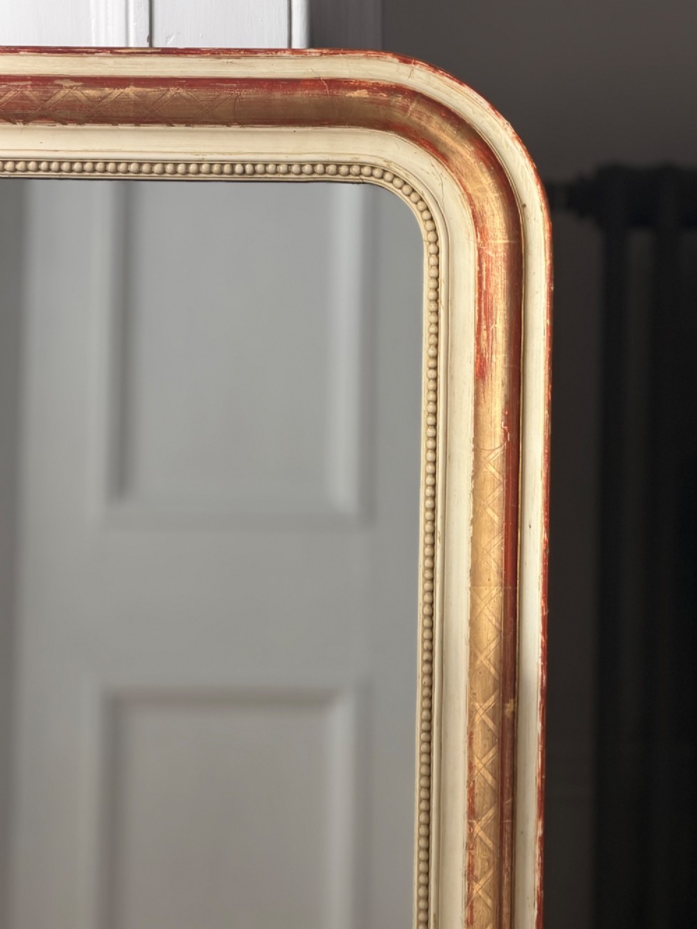 An antique French wall mirror with a rounded arched top, distressed gold leaf and cream gesso frame featuring incised geometric patterns and beaded inner edge. View VI