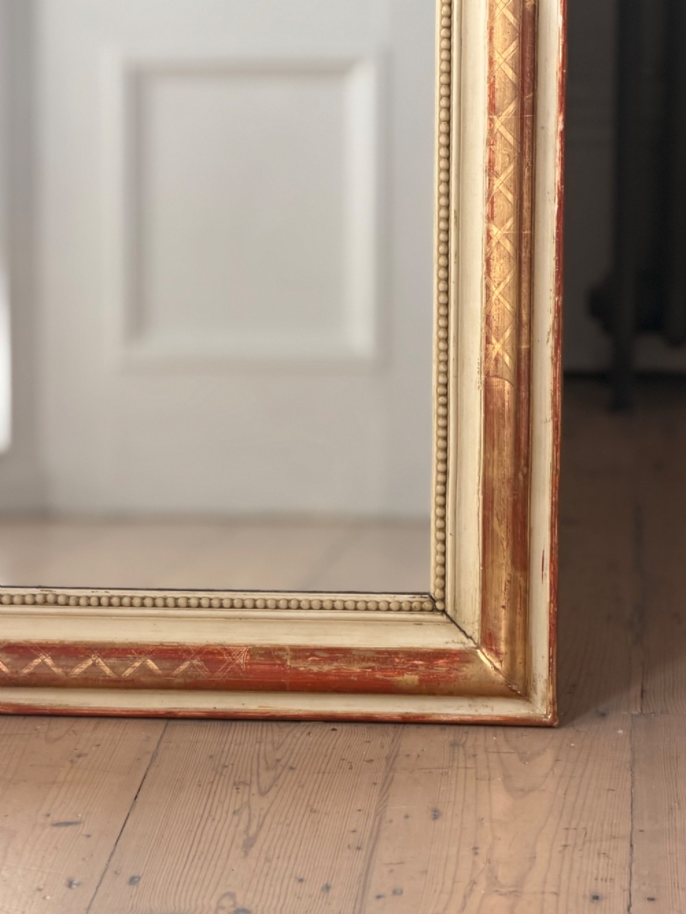 An antique French wall mirror with a rounded arched top, distressed gold leaf and cream gesso frame featuring incised geometric patterns and beaded inner edge. View VII