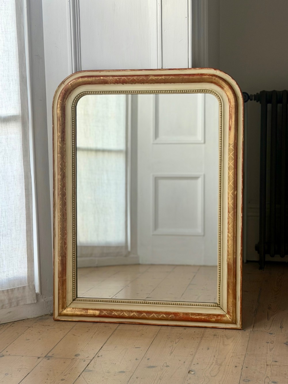 An antique French wall mirror with a rounded arched top, distressed gold leaf and cream gesso frame featuring incised geometric patterns and beaded inner edge. View IX